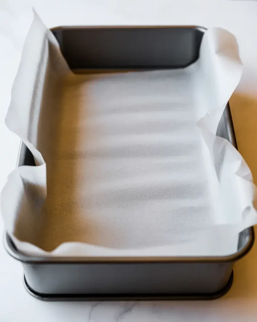 Metal baking pan lined with parchment paper showing overhangs for easy bar removal