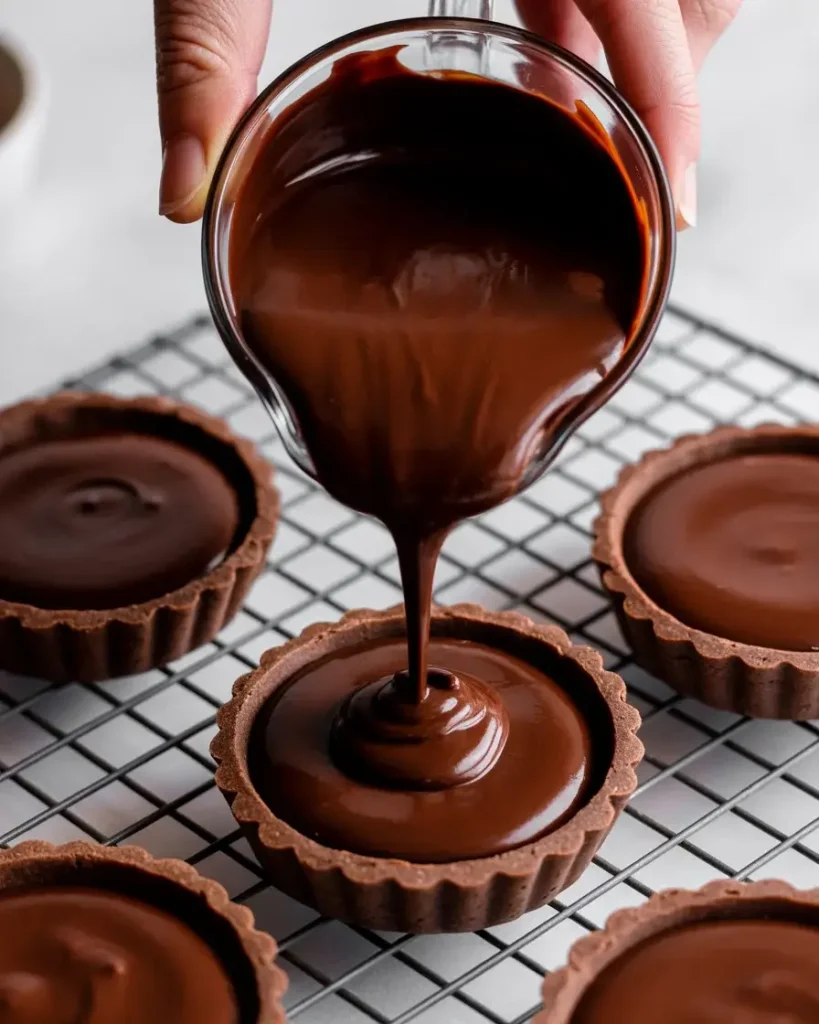 Pouring silky ganache into tartlet shells before chilling to set