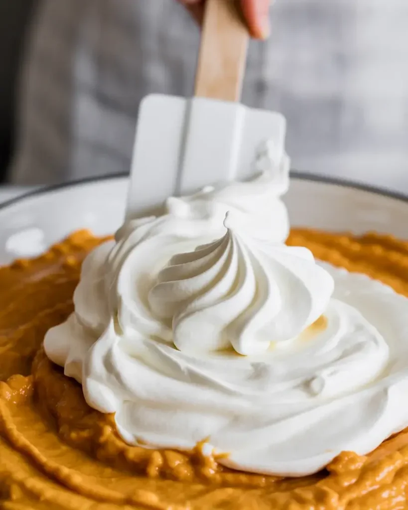 Gently folding whipped cream into pumpkin filling for a light mousse-like texture