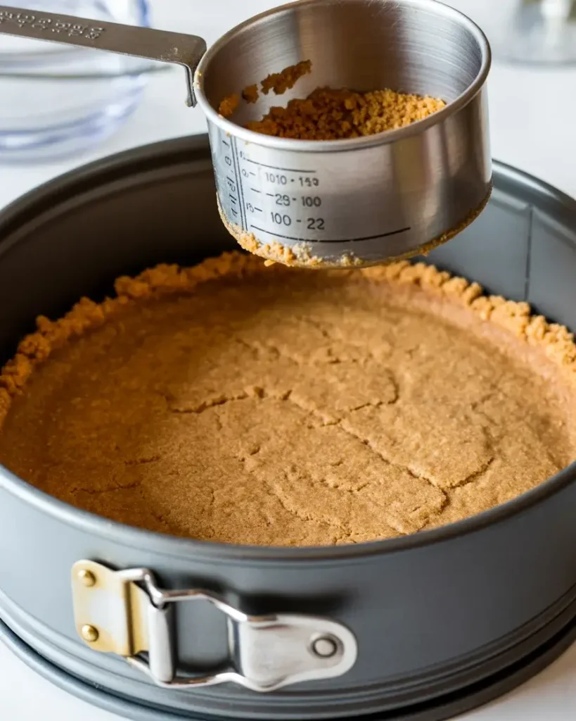 Pressing golden graham cracker crust firmly into springform pan for even base