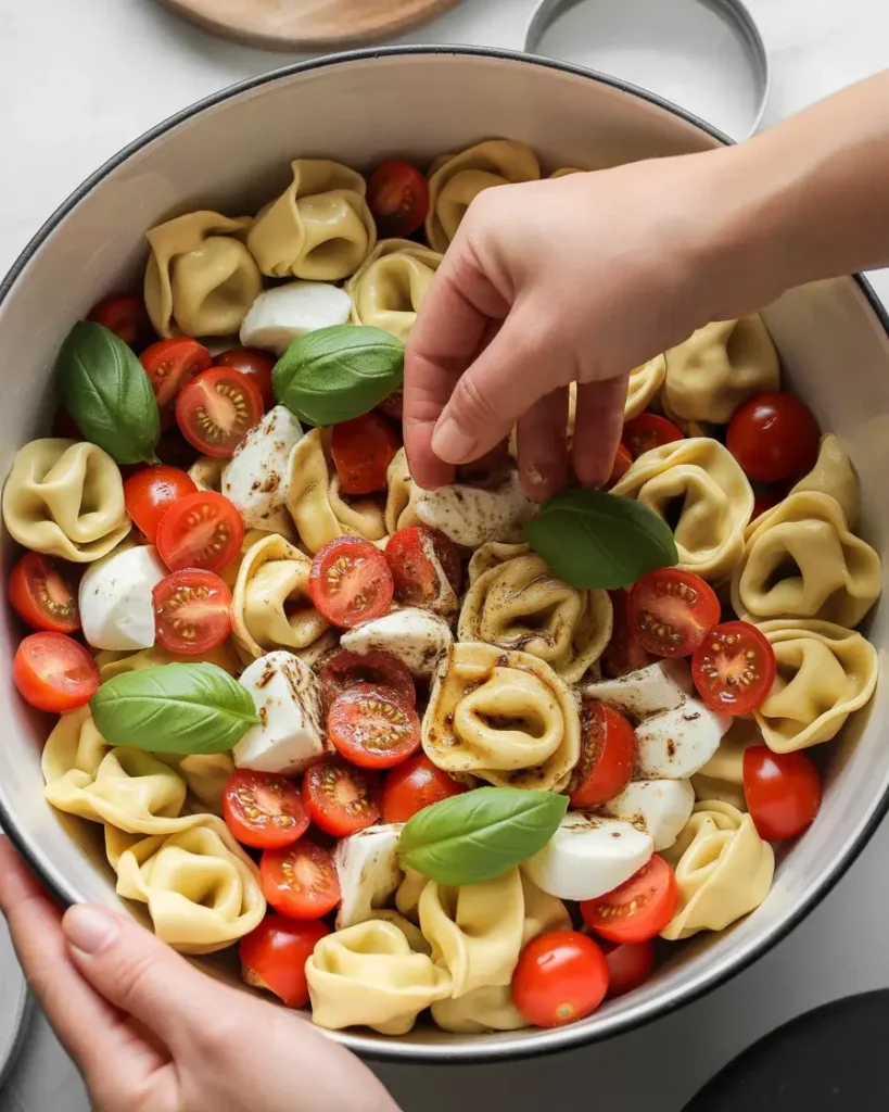 Gently folding tortellini with tomatoes, mozzarella, and torn basil in balsamic dressing